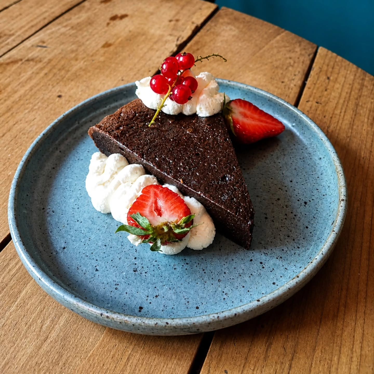 Part de fondant au chocolat servie sur une assiette bleue mouchetée, chantilly, fraises et groseilles