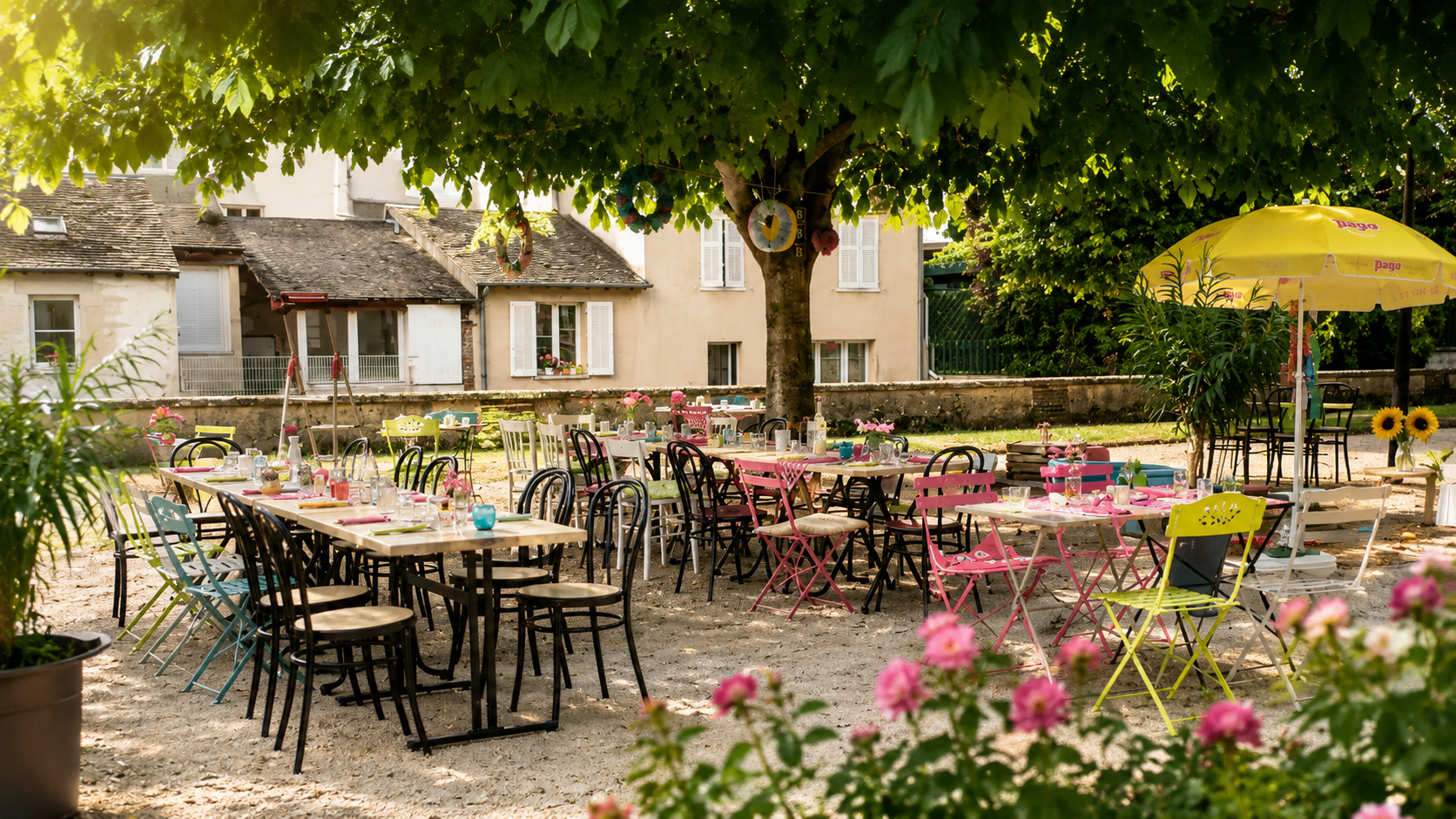 Terrasse de Chez les Sister's : tables en bois, chaises bistrot colorées et dépareillées, roses en fleur, sous l'ombre d'un grand arbre